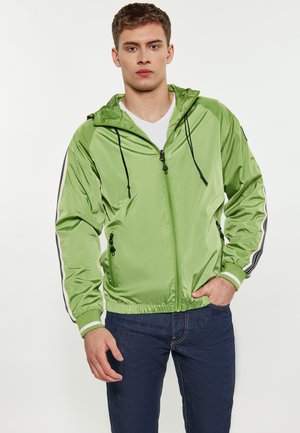 Grøn, letvægts zip-up jakke med hætte, der har sorte snoretræk, sidelommer og stribede detaljer på ærmerne.