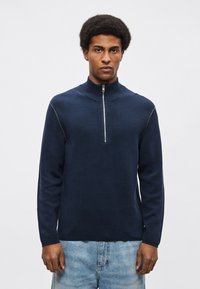 Tengerészkék pulóver magas gallérral, elöl cipzárral és kontrasztos varrással; puha, texturált anyagból készült.