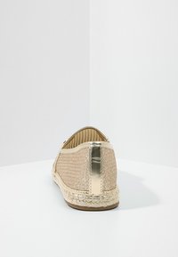 Bailarinas con parte superior de purpurina dorada, detalle metálico en la parte trasera, suela de esparto trenzado y forro interior beige. Textura suave.