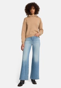 Beige Kapuzenpullover mit einem lässigen Schnitt, kombiniert mit hellblauen ausgestellten Jeans, die einen verwaschenen Look haben, und schwarzen Ankle Boots.