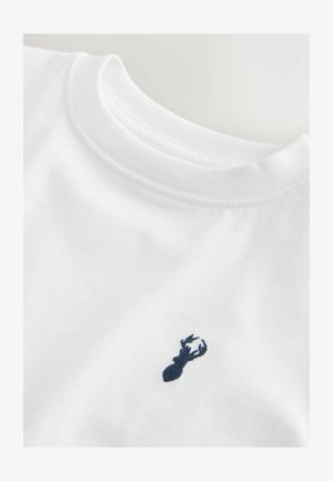 Tricou alb cu guler rotund, cu un mic logo brodat albastru închis reprezentând capul unui cerb în zona pieptului.
