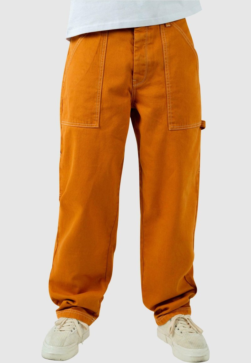 Pantalones cargo naranjas con corte holgado, que cuentan con múltiples bolsillos y costuras en contraste. Combinados con zapatillas blancas.
