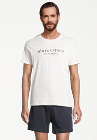 Biała bawełniana koszulka z okrągłym dekoltem z napisem "Marc O'Polo EST. W STOCKHOLMie" w kolorze szarym. Zestawiona z granatowymi szortami.