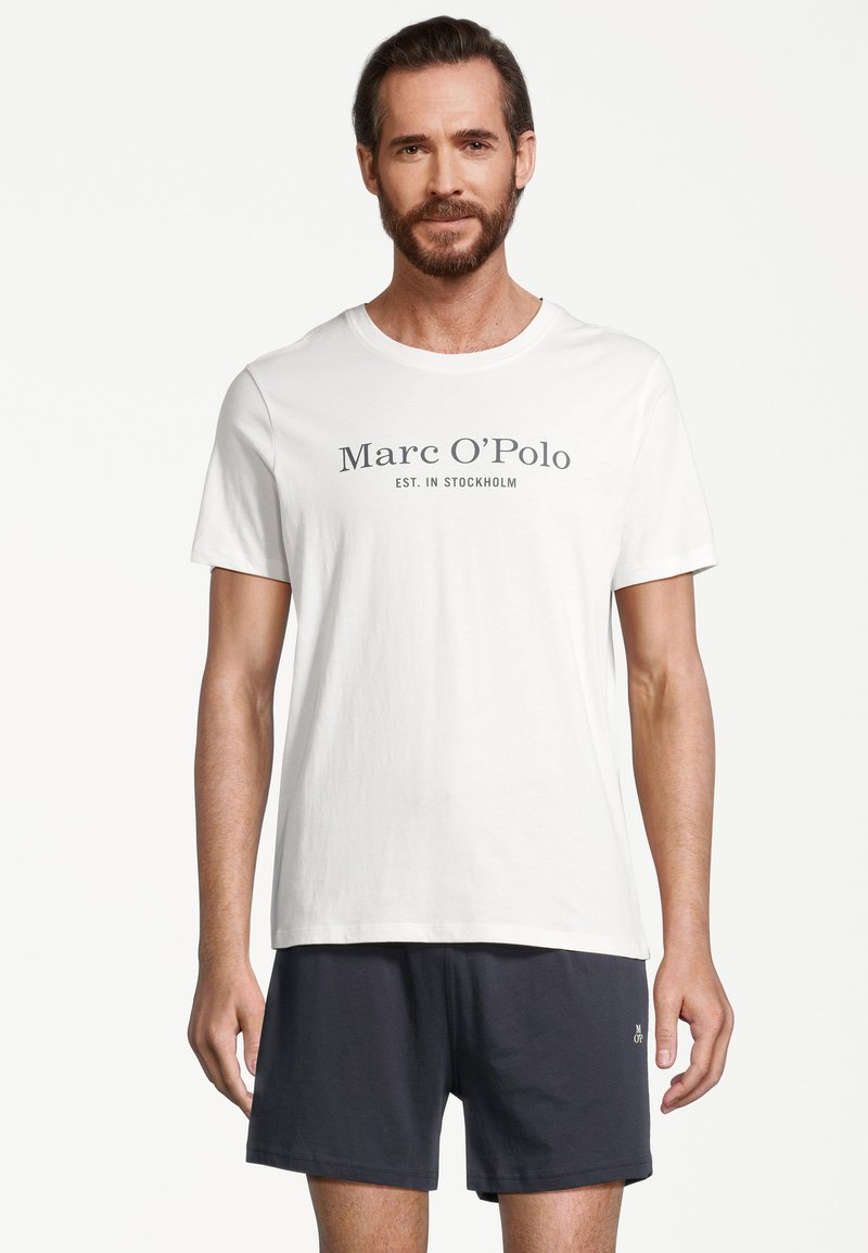 Biała bawełniana koszulka z okrągłym dekoltem z napisem "Marc O'Polo EST. W STOCKHOLMie" w kolorze szarym. Zestawiona z granatowymi szortami.