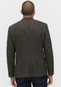 Brun tweedblazer med en texturerad tyg, enkel slits bak, och kn�äppta ärmslut, i kombination med en ribbad tröja vid ärmarna.