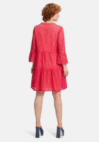 Rosa Spitzenkleid mit Glockenärmeln, gefächertem Design und rundem Ausschnitt, mit gewelltem Saum und transparenter Textur.