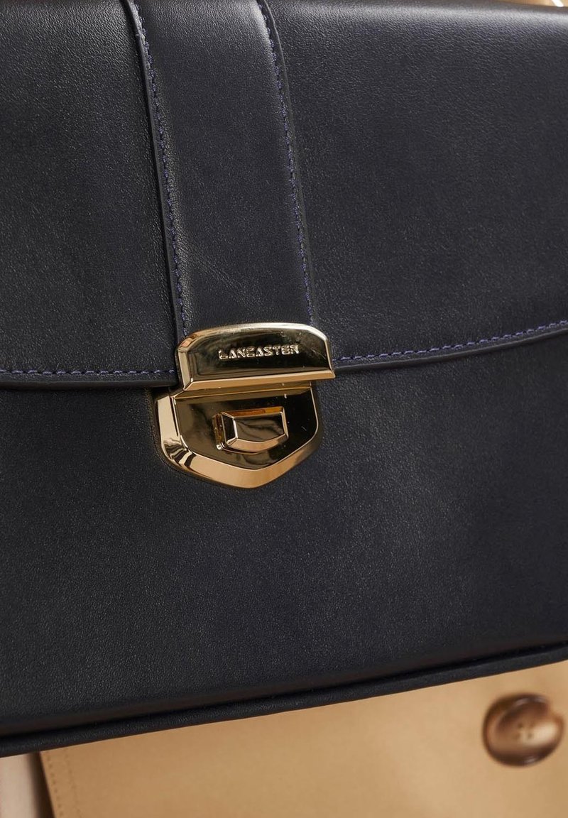 Dunkelblaues Lederhandtasche mit einem Goldtonverschluss. Sie verfügt über eine glatte Textur und ein kontrastierendes beiges Unterteil mit Druckknöpfen.