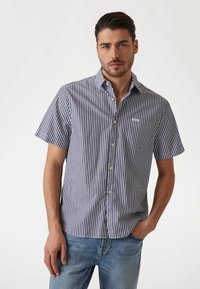Camisa de botones de manga corta en rayas azul marino y blanca, hecha de algodón, que cuenta con un bolsillo en el pecho y una pequeña etiqueta con el logo en el bolsillo.