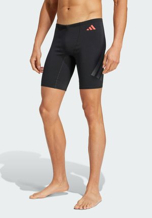 Pantaloni da nuoto neri realizzati in materiale elastico, con un design aderente, logo rosso a contrasto in vita e sottili strisce laterali.