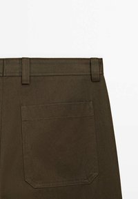 Mörkbruna bomullsbukser med en jämn textur, med en platt midja och en enda bakfickan med rundad botten.