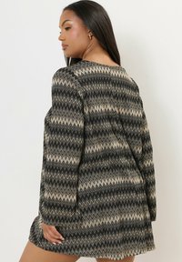 Korte jurk met een zwart en beige zigzagpatroon, lange mouwen, een ronde halslijn en een relaxte pasvorm, gemaakt van een lichtgewicht stof.