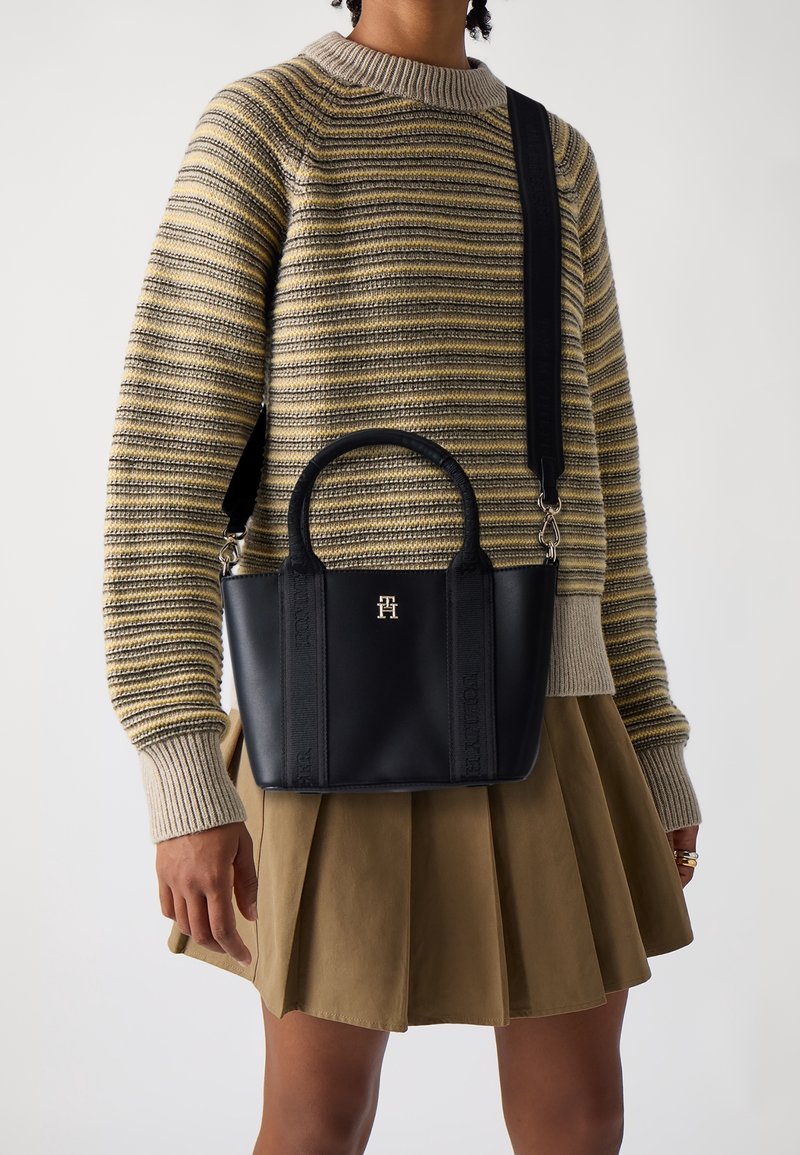 Zwarte leren tote bag met een gestructureerde vorm, dubbele handvatten en een afneembare schouderriem. Voorzien van een verhoogd logo en subtiele stikdetails.