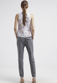 Ärm-lös topp med blommönster i ljuslila och krämfärg, kombinerad med grå tapered byxor och beige högklackade skor.