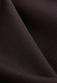 Gros plan d’un tissu brun foncé avec une texture côtelée fine et des plis doux créant des ombres et des reflets.