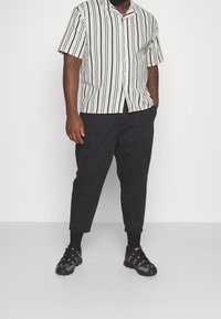 Vaaleanbeige-ja mustaruudullinen lyhythihainen paita, yhdistetty mustiin kapeanlahkeisiin housuihin ja mustiin urheilujalkineisiin, joissa on violetteja yksityiskohtia.