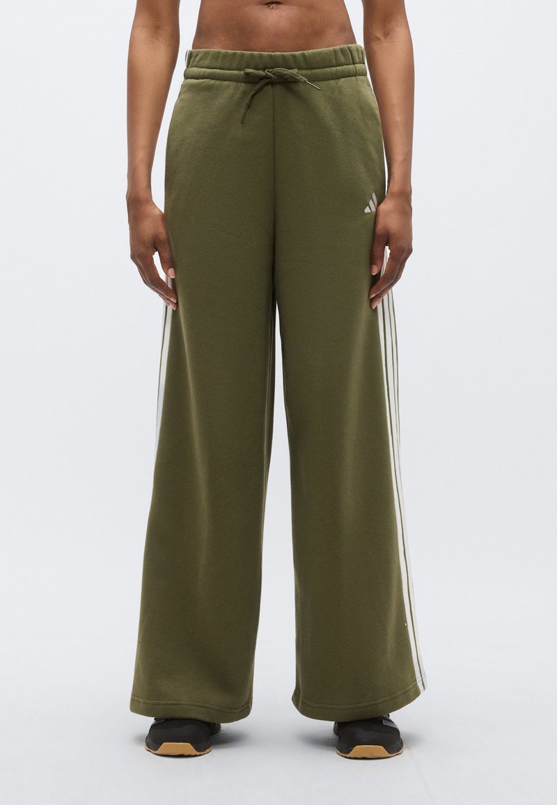 Zielone spodnie dresowe o szerokich nogawkach z regulowanym paskiem i białymi paskami po bokach. Materiał wydaje się miękki i gładki w dotyku.