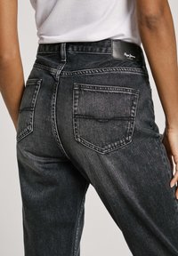 Svarta denimjeans med hög midja, avslappnad passform, två bakfickor och en läderlogotyp på midjebandet.