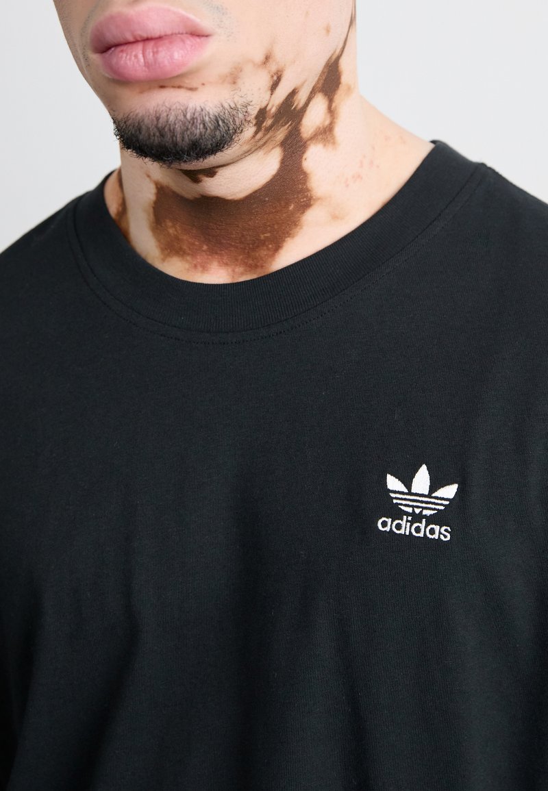 Schwarz Baumwoll-T-Shirt mit Rundhalsausschnitt, ausgestattet mit einem weißen gestickten Adidas-Trefoil-Logo auf der Brust, glatte Stofftextur.