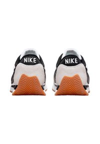 Sneaker Nike in bianco e nero con upper testurizzato, dettagli del tallone in contrasto e suole in gomma arancione con un motivo a zigzag.