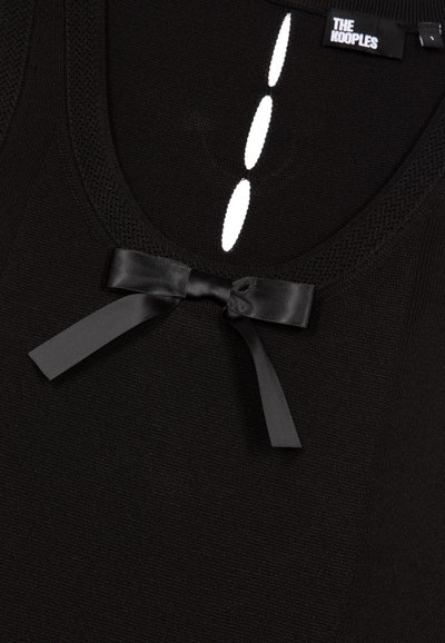 Débardeur noir avec un col en maille, un nœud en satin décoratif et des découpes blanches en forme de bouton sur le devant. Tissu lisse dans l'ensemble.