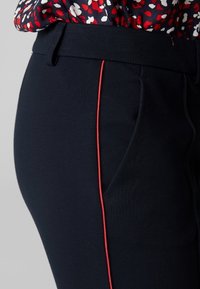 Pantalon bleu marine à coupe slim, avec des passepoils rouges et des poches sur le devant, fabriqué dans un tissu lisse et extensible.