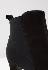 Bottine noire en combiné de cuir suédé et matière élastique, avec une finition texturée et un design épuré, mettant en valeur les détails de couture.