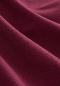 Bordeaux stof met een zachte, gladde textuur. Het materiaal valt elegant, met subtiele variaties in diepte en glans over het oppervlak.