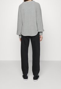 Pull en gris texturé avec un ourlet arrondi, porté par-dessus un pantalon noir ample et des chaussures noires, doté de poignets élastiques.