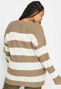 Stickad tröja med horisontella beige och vita ränder, ribbad textur, oversized passform och långa ärmar med tumhål.