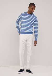 Maglione a righe blu e bianche in cotone con collo a giro, abbinato a pantaloni bianchi e sneakers blu navy. Texture morbida, vestibilità rilassata.