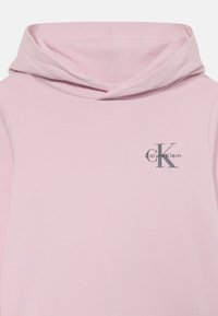 Felpa con cappuccio rosa realizzata in tessuto morbido. Presenta un piccolo logo grigio di Calvin Klein sul lato sinistro del petto. Design semplice e minimale.