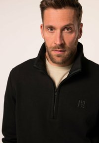 Chaqueta de forro polar negra con cremallera y un alto cuello, que presenta un logo sutil en el pecho y una textura suave. Diseñada para ofrecer calidez y comodidad.