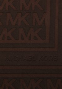 Ruskea tekstiili, jossa on kohokuvioitu geometrinen malli, joka esittää toisiinsa kietoutuvia "MK"-logoja, ja nimen "MICHAEL KORS" tasaisella, tummalla alueella alla.