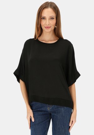 Czarny top z krótkim rękawem o szerokim, luźnym kroju, okrągłym dekoltem i gładkiej fakturze. Połączony z niebieskimi dżinsami o prostych nogawkach.