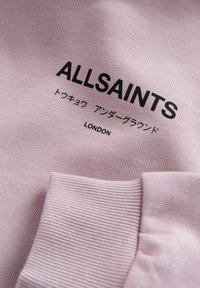 Tissu lavande avec le texte noir "ALLSAINTS", des caractères japonais en dessous, et "LONDON" imprimé au-dessus d'une bordure côtelée.