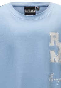Jasnoniebieska bawełniana koszulka z graficznym nadrukiem, na którym widnieją litery "R" i "M" w białym kolorze oraz "Memphis" napisane stylizowanym odręcznym pismem w dolnej części.