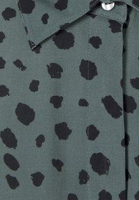 Groene stoffen shirt met een zwart luipaardprintpatroon, voorzien van een kraag en knoopsluiting. Soepele textuur met zichtbare stiksels.