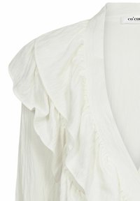Blusa bianca con dettagli arricciati lungo il colletto e la parte frontale, realizzata in un tessuto testurizzato e con un design a profondo scollo a V.