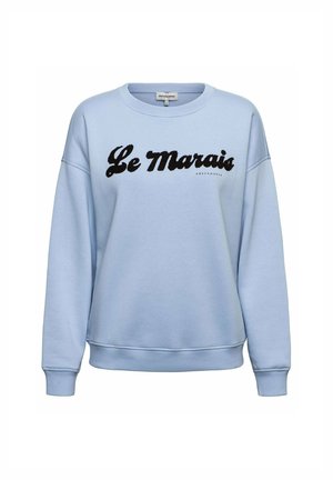 Lichtblauwe trui met zwarte cursief tekst "Le Marais" en kleine merknaam "ANDCOWOMAN" onder de tekst op de borst.