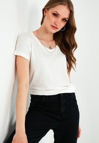 Hvid kortærmet t-shirt med rullede ærmer, parret med sorte jeans. Glat stof, afslappet pasform og enkelt design. Sølv lagdelt halskæde som accent.