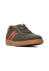 Zapatilla verde con acentos de cuero marrón, punta redonda, superficie texturizada y suela de goma. Cuenta con lengüeta acolchada y detalles de costura.
