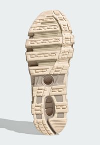 Bežová podrážka športovej obuvi s textúrovaným gumovým vzorom, ktorá obsahuje výrazné drážky pre trakciu a kontúrované výrezy pre flexibilitu.