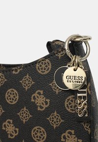 Borsa a tracolla sintetica nera con texture, caratterizzata da un motivo a logo marrone. Include un charm in metallo con incisione "GUESS EST.1981". Finiture in tonalità argentata.