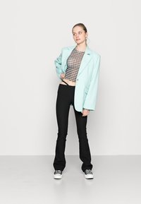 Blazer oversized verde menta, top cropped xadrez, calças pretas justas com flare e ténis clássicos pretos com solas brancas.