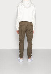 Bílá krátká mikina s kapucí a olivově zelené cargo kalhoty s bočními kapsami, v uvolněném střihu, doplněné bílými teniskami.