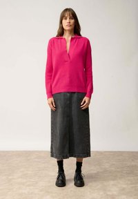 Rosa Strickpullover mit V-Ausschnitt, kombiniert mit einem grauen Jeansrock. Schwarze Schnürschuhe und schwarze Socken runden das Outfit ab.