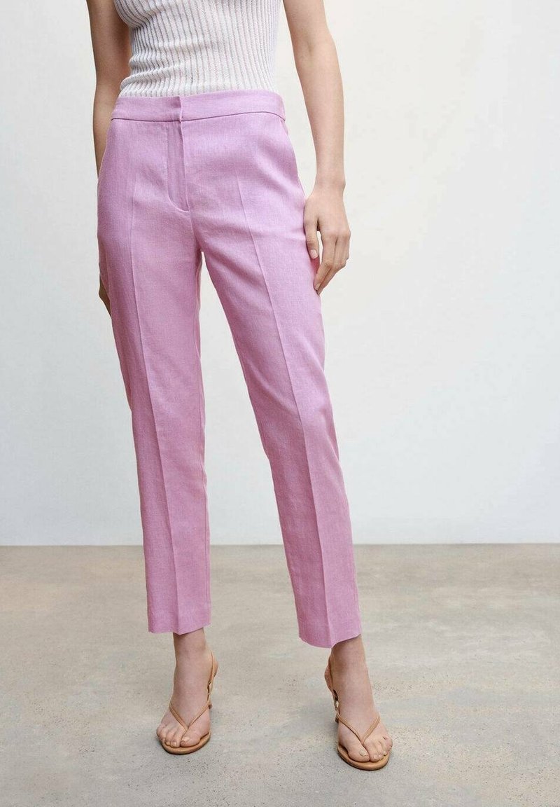 Frau in hochgeschnittenen, geraden pinkfarbenen Hosen, mit einem weißen ärmellosen, gerippten Oberteil und beigen, geschnürten Absatzsandalen.