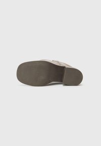 Chaussure en cuir marron avec un talon épais et une semelle en caoutchouc texturée. Le dessous présente une finition lisse et un motif subtil.