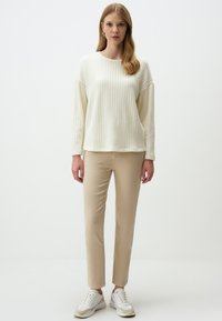 Pull en tricot texturé crème, pantalon beige ajusté, baskets blanches. L'ensemble présente une silhouette décontractée et un design côtelé sur le pull.