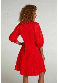 Rode katoenen jurk met een gelaagde rok, pofmouwen en een getailleerde taille. Soepele textuur en knielange ontwerp.
